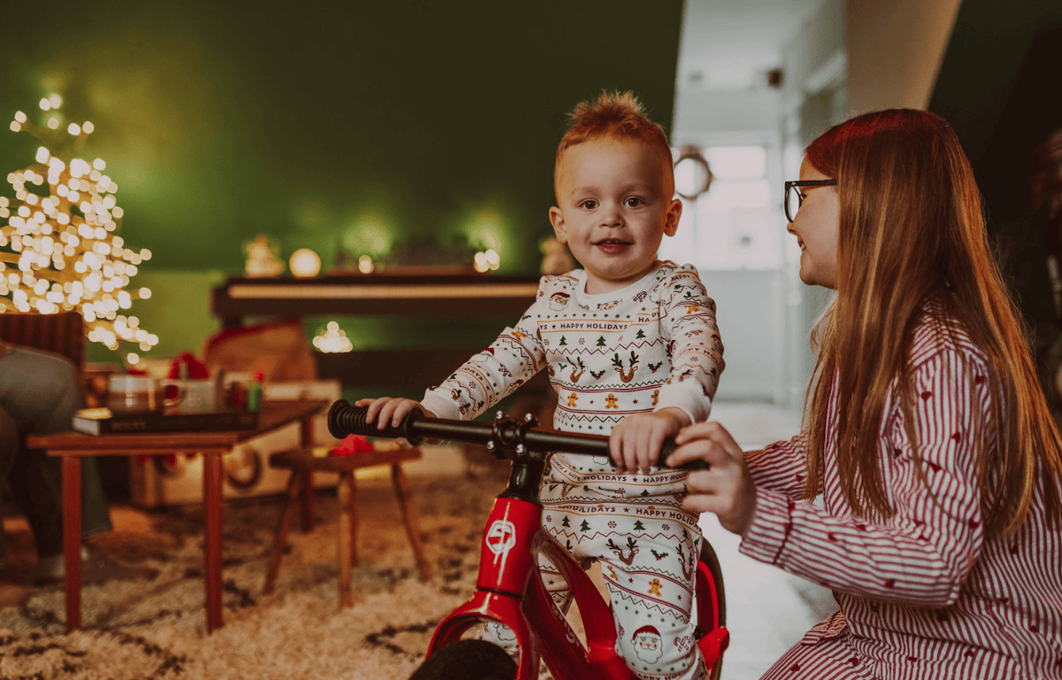 a child sits happily on his red shyre myndie bike with his mum nearby
